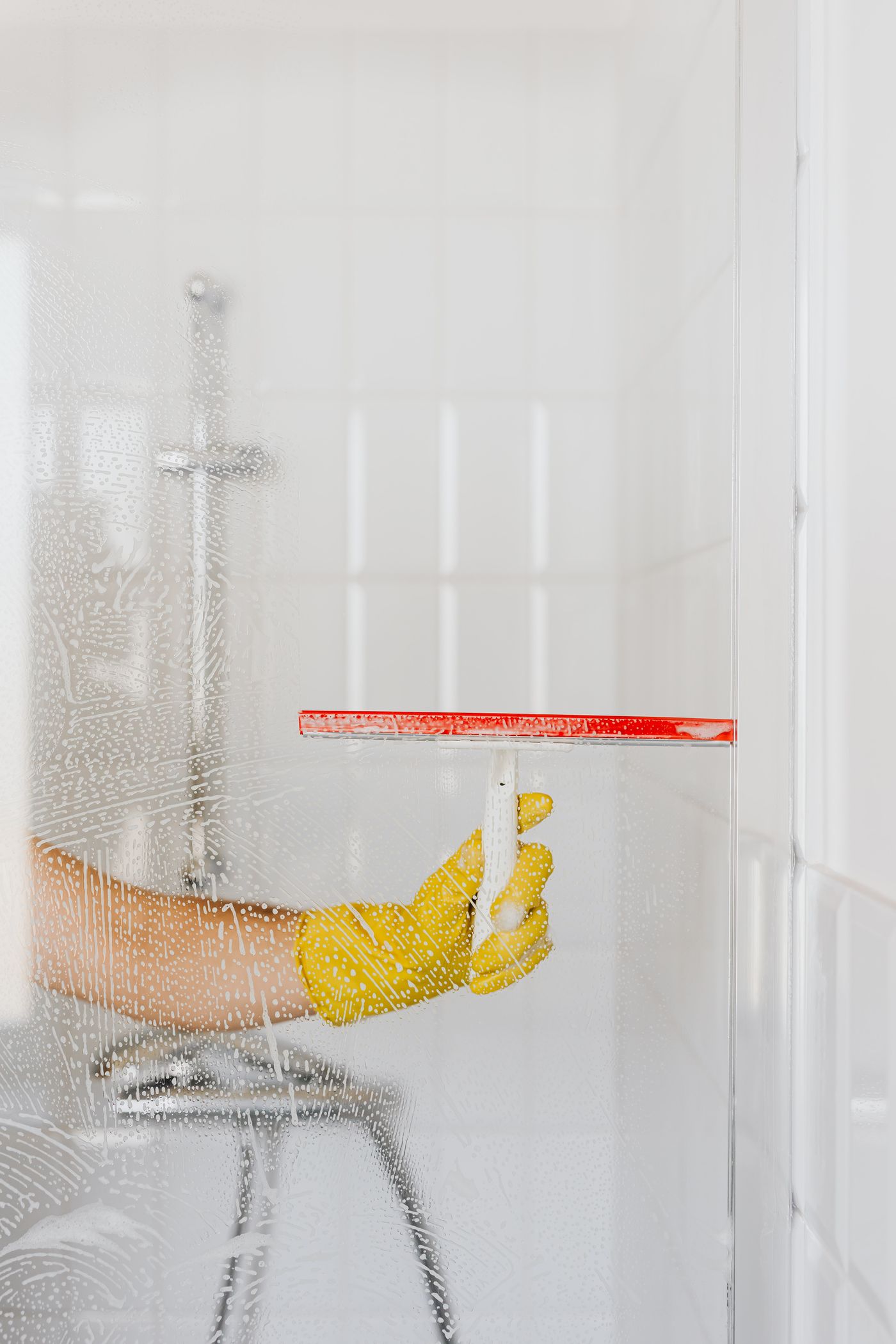 Representative stock photo of a person cleaning a glass shower with a squeegee