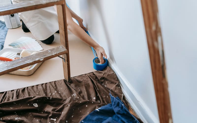 Representative stock photo of painter's tape being applied along interior trim before painting